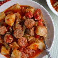 Italian sausage stew with potatoes and green beans in a tomato garlic sauce served in white serving bowl